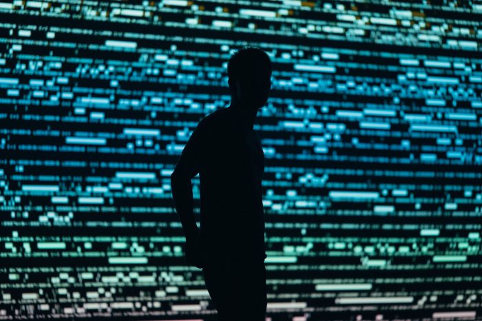 Dark figure standing in front of colorful lights 